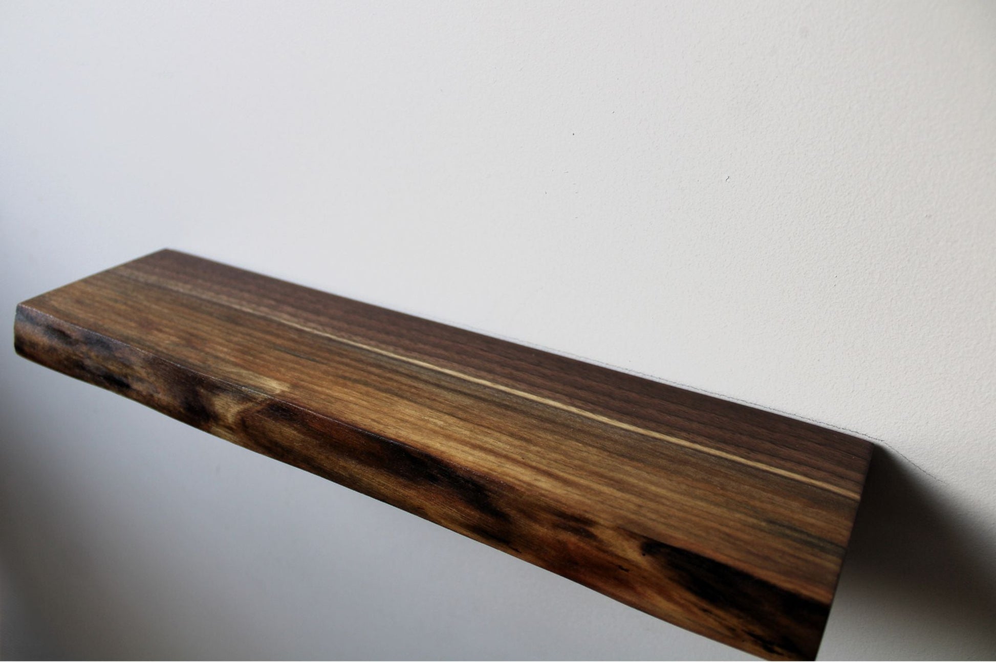 Solid walnut floating shelf mounted on wall, minimalist modern design